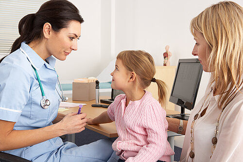 A nurse tending to a child patient, who is sitting on her mothers lap.