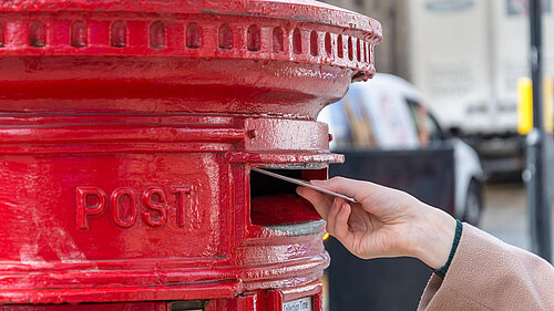 A woman posting a letter into a post box.